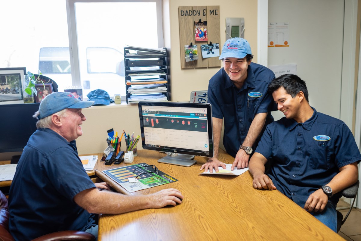 Three HVAC technicians smiling and laughing together in the West Coast Air Conditioning office